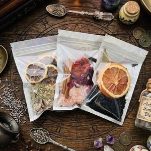 May include: Three clear resealable plastic pouches containing botanical ingredients. The first holds dried citrus slices and herbs, the second contains cinnamon sticks and pink salt, and the third features a dried orange slice over black salt.