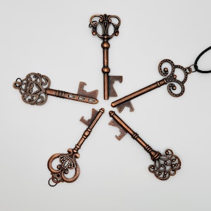 May include: Five bronze-colored key-shaped bottle openers arranged in a starburst pattern. Each opener features ornate detailing and a key-shaped design, with a bottle opener function at the base. One opener is attached to a black cord.