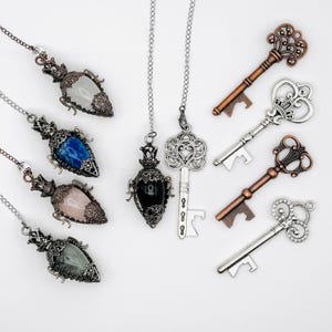 Puede incluir: Una colección de cuatro colgantes de piedras preciosas en forma de lágrima en cadenas plateadas, un colgante de piedra negra en cadena plateada, un colgante en forma de llave plateada en cadena y cuatro abridores de botellas decorativos en forma de llave en tonos cobre y plata.