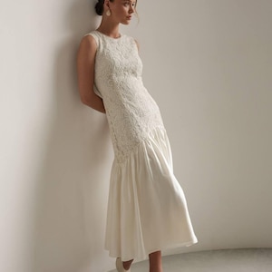 May include: A sleeveless ivory dress with intricate lace detailing on the bodice and a flowing skirt. The dress features a subtle fishtail hem and is paired with matching pointed-toe heels. The overall style is elegant and suitable for special occasions.
