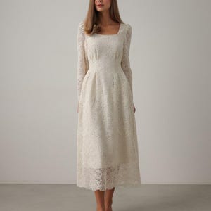 May include: A white lace dress with a square neckline and long sleeves. The dress has a fitted bodice and a flowing skirt.
