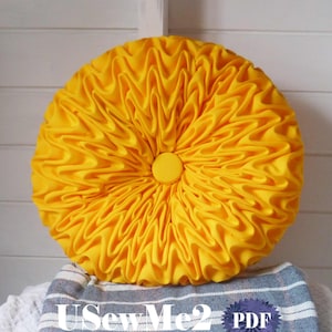 Könnte beinhalten: Ein rundes, leuchtend gelbes Kissen mit einem Knopf in der Mitte. Das Kissen besteht aus Stoff mit einer gerüschten Textur.