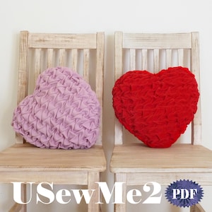 Könnte beinhalten: Zwei herzförmige Kissen, eines rosa und eines rot, liegen auf zwei Holzstühlen. Die Stühle sind weiß gestrichen und haben eine Lattenrücklehne. Die Kissen sind aus einem gekräuselten Stoff gefertigt. Der Text "USewMe2 PDF" ist unten in der Mitte des Bildes sichtbar.
