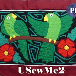 May include: A colorful, hand-stitched wall hanging featuring two green parrots perched on a branch with red flowers and green leaves. The background is black with a geometric pattern. The text "USewMe2" is at the bottom of the image.