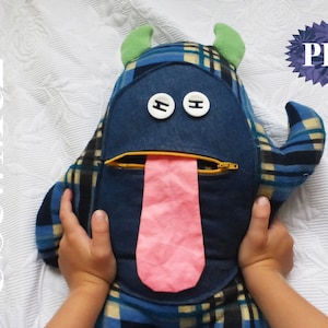 May include: A blue and plaid monster toy with a pink tongue sticking out of a yellow zipper. The monster has two green horns and two white buttons for eyes.