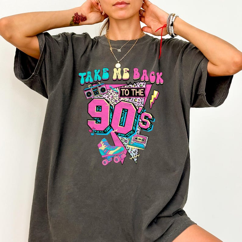 May include: Dark gray t-shirt with a colorful graphic design. The design features the text "TAKE ME BACK TO THE 90'S" with images of a boombox, roller skates, and a cassette tape. The shirt has a vintage, retro style.