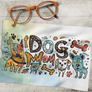 Könnte beinhalten: Ein weißes Mikrofasertuch mit der Aufschrift "DOG MOM" und Cartoon-Hunde-Illustrationen. Das Tuch hat einen Aquarellhintergrund und wird mit einer Brille mit Holzrahmen kombiniert.