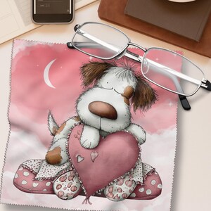 Könnte beinhalten: Ein rosa Mikrofasertuch mit einem Cartoon-Hund, der ein rosa Herz hält. Der Hund hat braunes und weißes Fell vor einem rosa Wolkenhintergrund mit einem Halbmond. Eine Brille mit silbernem Rahmen liegt auf dem Tuch.