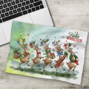 Könnte beinhalten: Ein Mikrofasertuch mit einem festlichen Design mit sechs Rentieren, die mit Weihnachtsdekorationen geschmückt sind und Geschenke tragen. Das Tuch hat einen grün-blauen Aquarellhintergrund mit Schneeflocken und dem deutschen Text "Frohe Weihnachten!" in Rot.