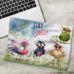 Könnte beinhalten: Ein weißes Mikrofasertuch mit einer skurrilen Illustration von vier Cartoon-Vögeln mit ausdrucksstarken Augen und farbenfrohem Gefieder. Auf dem Tuch steht der Text "STAY CRAZY". Ein Laptop ist teilweise im Bild zu sehen.
