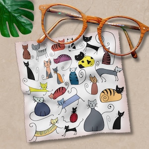 Könnte beinhalten: Ein weißes Mikrofaser-Reinigungstuch mit rosa Rand zeigt ein fantasievolles Design mit bunten Katzen in verschiedenen Ausdrücken und Posen. Die Katzen sind in einem einfachen, cartoonartigen Stil gezeichnet.