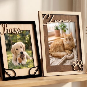 May include: Two rectangular wooden picture frames with personalised names. The left frame is black with light wood accents and angel wings, displaying a puppy. The right frame is dark wood with light wood accents and a paw print, displaying a cat.
