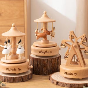 Könnte beinhalten: Drei hölzerne Spieluhren: ein Karussell mit einem Pferd, ein Riesenrad und eine Spieluhr mit Ballerina-Motiv. Das Karussell hat ein Pferd und zwei weitere Tiere. Das Riesenrad hat sechs Gondeln. Die Ballerina-Box hat drei Ballerinas.