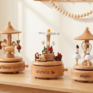 May include: Three wooden carousel music boxes with different themes. One features horses, another a winter scene, and the third ballerinas. Each box has a name engraved on it: Oliver, Victoria, and Bblythe.