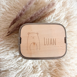 Könnte beinhalten: Eine Lunchbox aus Holz mit einem Edelstahlrand. Der Deckel ist mit einem Bären und dem Namen "LUAN" graviert.