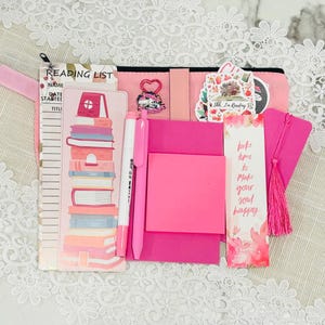 May include: Pink reading list tracker with a pink and white stack of books illustration, a pink pen, a pink sticky note, and a pink bookmark with the text "take time to make your soul happy".