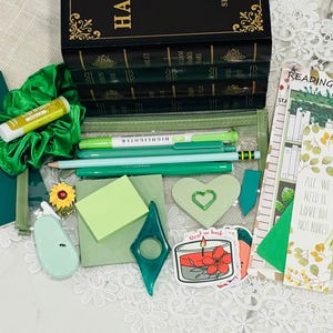 May include: An assortment of green stationery and accessories, including pens, pencils, a highlighter, a scrunchie, and a bookmark with the text "ALL WE NEED IS LOVE BUT NOT NUKES". Also includes a green journal, stickers, and a heart-shaped patch.