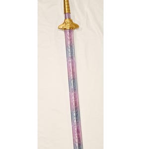May include: A decorative sword with a gold handle and guard, and a purple and gray blade. The handle features ornate detailing and a floral design. The blade has a textured pattern.