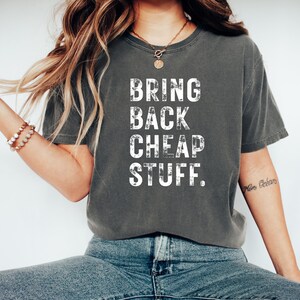 May include: A dark gray t-shirt with the text "BRING BACK CHEAP STUFF." printed in white on the front.