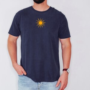 May include: Navy blue t-shirt featuring a yellow sun design on the chest. The short-sleeved shirt is made of a soft material and is suitable for casual wear. The sun graphic has a simple, stylized design.