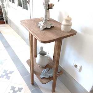 Peut inclure: Petite table d'appoint en bois brun clair avec une étagère inférieure. La table supporte un candélabre blanc, un petit pot blanc, une cruche blanche et une feuille décorative. La table mesure 71 cm de haut.
