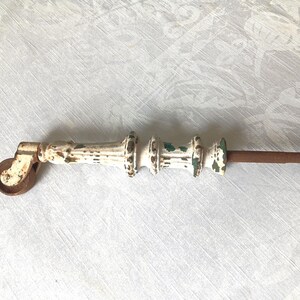 Peut inclure: Une roulette de meuble ancienne dotée d'un corps en métal peint en blanc avec de la peinture écaillée révélant de la rouille. La roulette présente une colonne centrale cannelée avec trois anneaux décoratifs et une roue en métal brun.