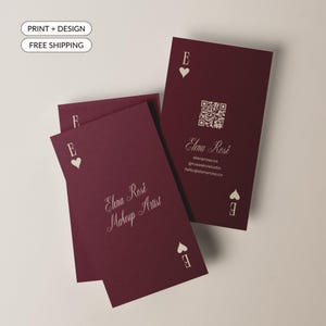 May include: A set of rectangular business cards in deep burgundy with a playing card aesthetic. The cards feature a white heart icon, the letter E, and the text Elena Rosé Makeup Artist. One card displays a QR code, website, and email address.
