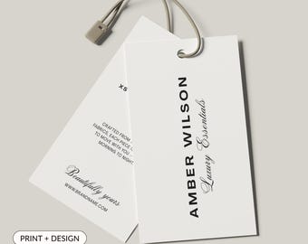 May include: Two white rectangular product tags with a beige string. One tag reads "AMBER WILSON Luxury Essentials" in black text. The other tag has the text "Beautifully yours" and "Crafted from fabrics, each piece..."