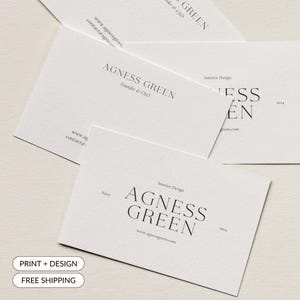 May include: A collection of white business cards with the text "AGNESS GREEN" in a minimalist design. The cards also include the text "Interior Design", "Founder & CEO", and a website address. The cards are arranged on a light-colored surface.