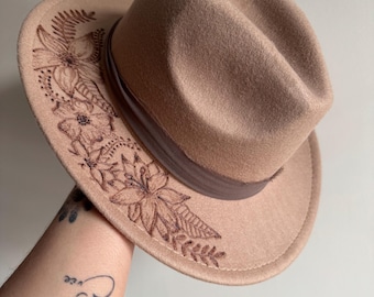 May include: A brown felt fedora hat with a floral design embroidered around the brim.