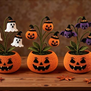 May include: Three crocheted potted plants in orange jack-o'-lantern bases. The first features white ghosts wearing black witch hats, the second has orange pumpkins with hats, and the third displays purple bats with hats, all with green stems and leaves.