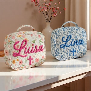 May include: Two quilted, square bags with handles. One is white with a floral pattern and the name "Luisa" in pink script, plus a pink cross. The other is blue with a floral pattern and the name "Lina" in blue script, plus a blue cross.