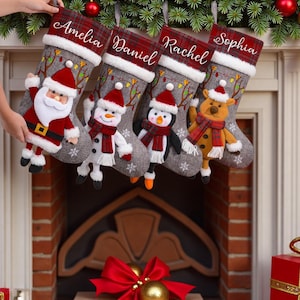 May include: Four Christmas stockings with personalized names: Amelia, Daniel, Rachel, and Sophia. Each stocking features a different plush character: Santa Claus, a snowman, a penguin, and a reindeer. The stockings have a gray background with snowflake patterns and red plaid accents.