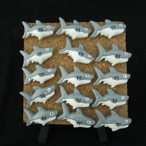 15 Great White Shark Push Pins. They are about an inch long and 1/2 inch high. They come in a metal box with window.