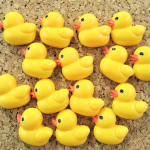 May include: A collection of fourteen small, bright yellow rubber ducks arranged in a grid. Each duck features a smooth, rounded body, a small orange beak, and a single black dot for an eye. The ducks are uniform in size and color, displaying a classic duck shape with a raised tail and head.