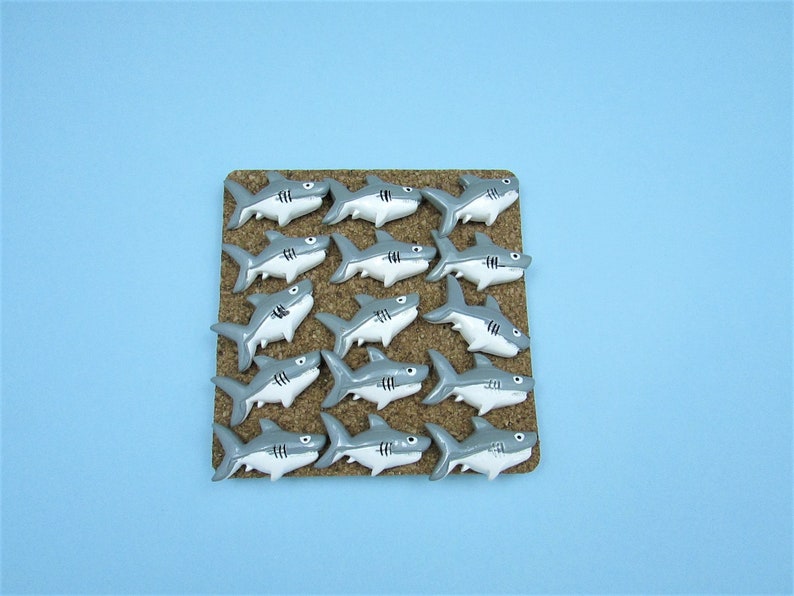 15 Great White Shark Push Pins. They are about an inch long and 1/2 inch high. They come in a metal box with window.