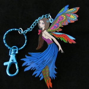 May include: A keychain featuring a blue metal ring and lobster clasp attached to a flat, illustrated charm of a fairy. The fairy has brown hair, a purple top, a blue skirt, and large, multicolored wings with intricate patterns.
