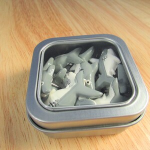 15 Great White Shark Push Pins. They are about an inch long and 1/2 inch high. They come in a metal box with window.
