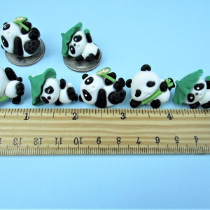 15 Pandas playing with bamboo. Some are wearing leaf hats and holding bamboo and bamboo shoots. Each panda is about 1 inch tall. They come in a metal box with window.