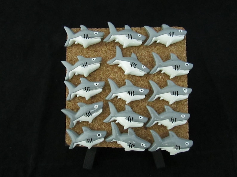 15 Great White Shark Push Pins. They are about an inch long and 1/2 inch high. They come in a metal box with window.