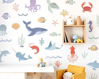 May include: A white wall adorned with cartoon sea life stickers, such as whales, fish, and an octopus. A small yellow chair and a white table are in the foreground. A wooden shelf displays books and toys.