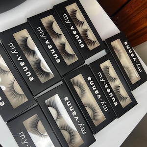Könnte beinhalten: Mehrere schwarze Boxen mit durchsichtigen Fenstern, in denen Paare von falschen Wimpern zu sehen sind. Jede Box trägt den Aufdruck "my.vanna".