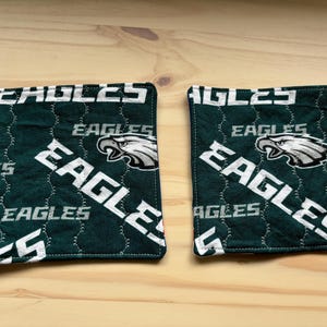 May include: Two green and white quilted pot holders with the Philadelphia Eagles logo and the word "Eagles" repeated on them.