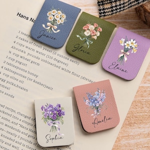 May include: Five leatherette bookmarks, each with a floral bouquet design and a name. The bookmarks are in various colors: blue, green, purple, beige, and pink. The names are Janice, Gloria, Elaine, Sophia, and Amelia.