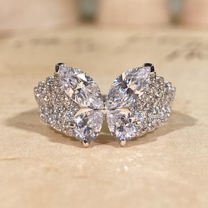 May include: A silver-toned ring featuring a butterfly design composed of two marquise-cut stones at the top and two pear-cut stones at the bottom, with the wings and band encrusted with numerous small, clear, round-cut pavé stones.