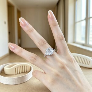 May include: A silver-toned ring featuring a large rectangular radiant-cut center stone flanked by two smaller baguette-cut stones on each side, set on a thin band adorned with small pav&eacute;-set stones along the visible portion of the shank.