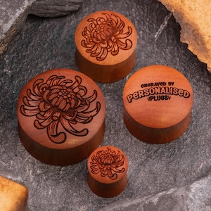 May include: Four wooden ear gauges featuring a floral design. The gauges are engraved with the text "Engraved by Personalised Plugs".