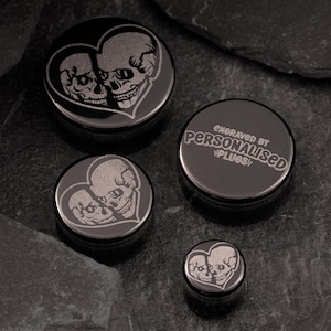 Könnte beinhalten: Satz von drei schwarzen Ohrdehnern mit einem herzförmigen Design mit zwei Schädeln. Der größte Dehner ist mit dem Text "Engraved by Personalised Plugsy" graviert.