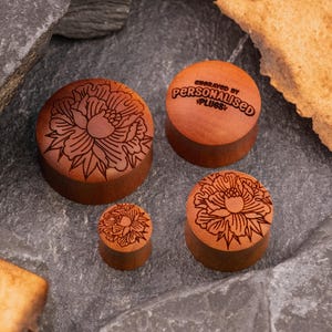 May include: Four wooden ear gauges with a floral design. The largest gauge has the text "Engraved by Personalised Plugs" on it.