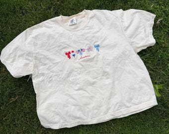 Camiseta corta holgada con bordado de iconos estadounidenses, color marfil, para mujer, ideal para el 4 de julio.